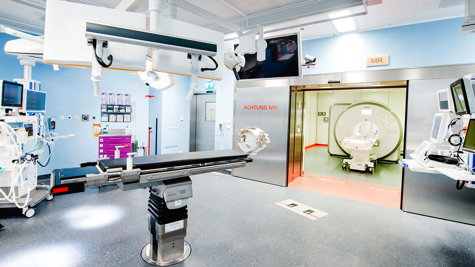 Operationssaal mit Operationstisch im Vordergrund und Hochfeld-MRI in direkter Anbindung zum OP im Hintergrund